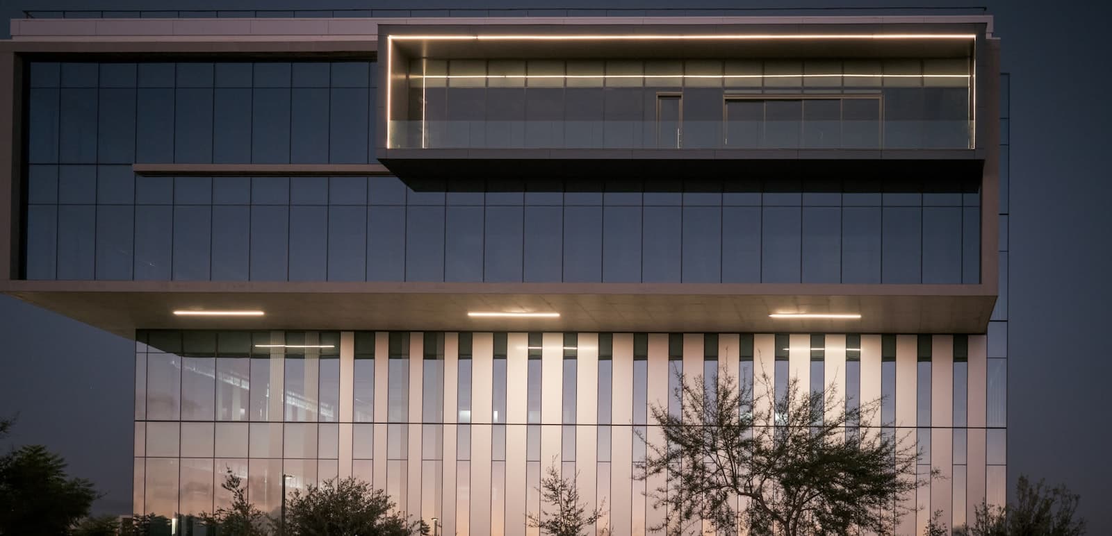 Corporate office building with a lit glass facade at dusk.